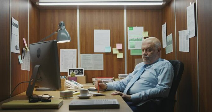 Bored inefficient employee sitting at his desk in a small office and wasting time