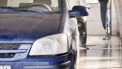 Car wash worker cleaning dirty blue car with high pressure water jet