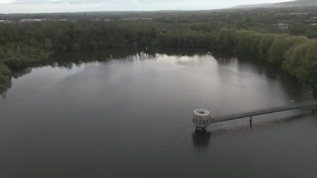 Drone shot of a reservoir at dusk, with a sci looking 1960s or 70s intake tower
