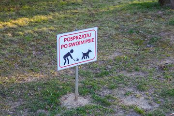 Red Warning Sign for Pet Owners About Picking Up After Dogs on Grassy Area
