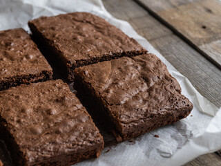 Freshly made brownie cut into portions on baking paper on a wooden table