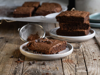 A slice of chocolate brownie garnished with cocoa and sprinkles. A stack of brownies in the...