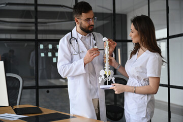 Holding model of human spine. Two doctors are in the office