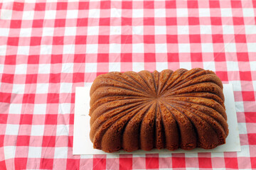 Bolu gula aren. Delicious brown butter cake with elegant swirl pattern on top, placed on a red checkered tablecloth outdoors with green grass in the background—perfect for picnic or rustic food themes