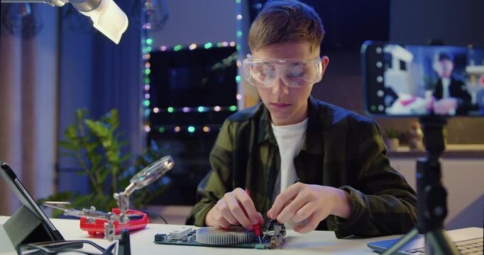 Boy in glasses with a tool repairs a home electronic appliance. Male professional boy repairs a computer. Engineer soldering microcircuit.