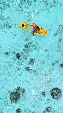 woman in a bikini relaxes on a yellow kayak floating on clear turquoise sea, top-down view from above, peaceful moment in tropical paradise, summer holiday, maldives, travel, holidays, vacation