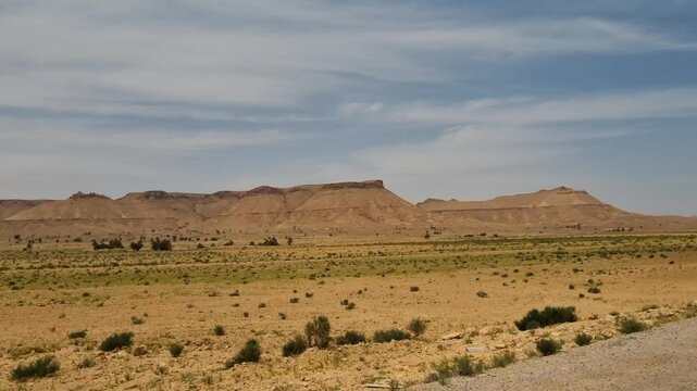 Shot from a moving car, capturing the expansive and arid Saharan desert landscape in southern Tunisia on a partly cloudy spring day