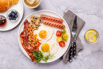 A classic breakfast plate featuring sunny-side-up eggs, crispy bacon, sausages, and fresh tomatoes