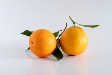 Two fresh, rich and healthy oranges with leaf resting on white background