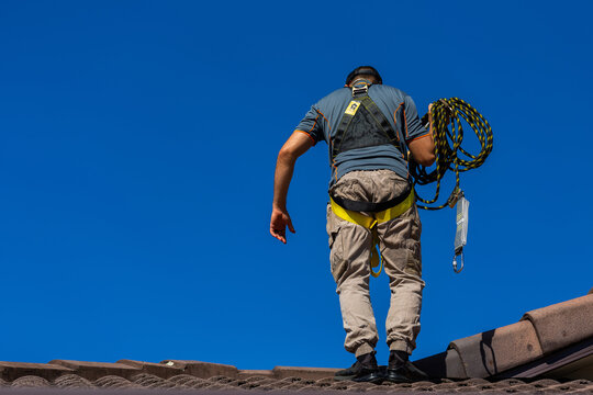 Tradie climbing on roof of house in safety harness to secure rope for safety compliance