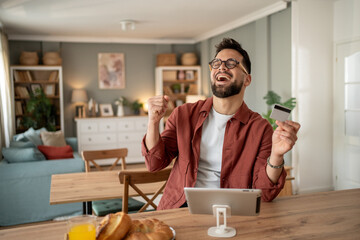Excited man using tablet and credit card for online shopping at home