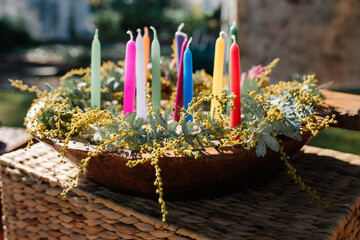 Colourful candles in a dish with yellow flowers.