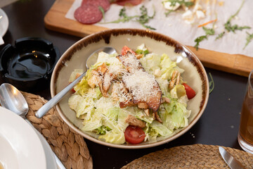 Fresh Caesar salad served in a rustic bowl featuring crisp lettuce, grilled chicken, croutons, cherry tomatoes, and generous grated Parmesan cheese. A classic restaurant favorite.