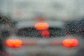 Raindrops on car window with defocused red lights from traffic in the background, essence of rainy...