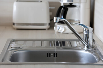 Water flows from a shiny faucet in a modern cozy kitchen interior.