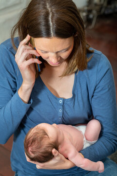Mother holding newborn baby and talking on phone