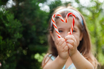 Little girl holding candy cane sweets in heart shape outside near pine tree
