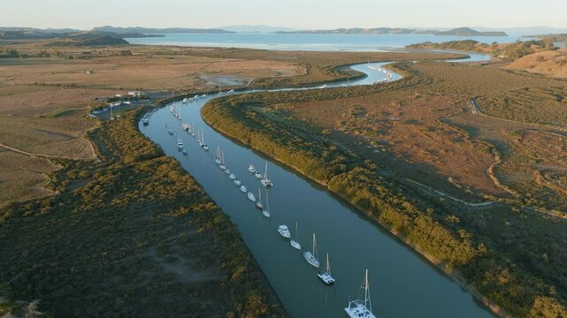 Aerial view of sailboats moored along a river in a rural landscape. The boats are lined up, reflecting in the calm water. Taken in New Zealand. CLEVEDON, NZ