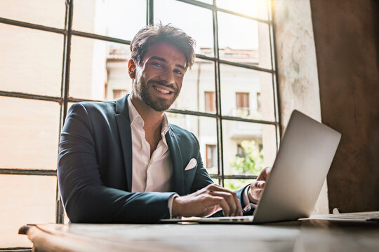 Confident young businessman smiling at camera while working with laptop