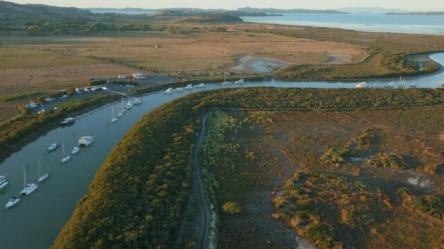 Aerial view of sailboats moored along a river in a rural landscape. The boats are lined up, reflecting in the calm water. Taken in New Zealand. CLEVEDON, NZ