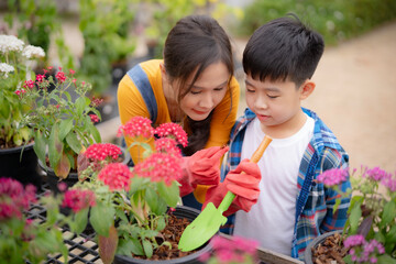 Young Asian mother and son doing gardening by watering flower. Beautiful woman and boy using watering pot in garden with happiness.