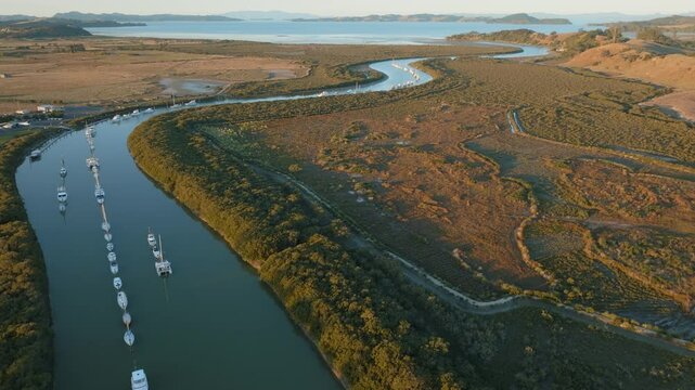 Aerial view of sailboats moored along a river in a rural landscape. The boats are lined up, reflecting in the calm water. Taken in New Zealand. CLEVEDON, NZ
