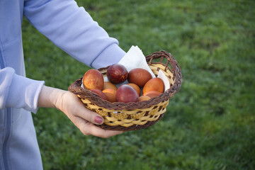 Person's hands hold a wicker basket filled with colorful Easter eggs, ready for celebration.