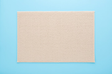 Light brown new soft home carpet on light blue table background. Pastel color. Closeup. Top down view.