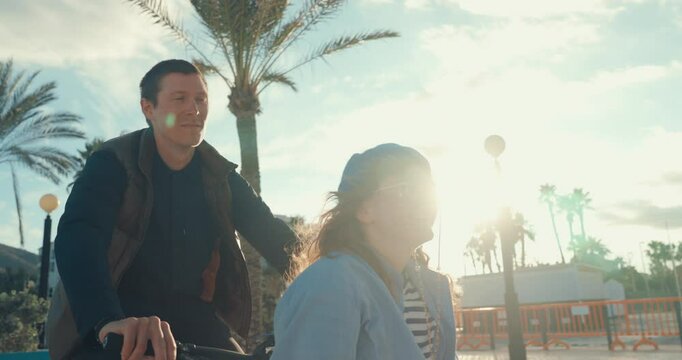Happy candid couple ride on cargo bicycle on promenade on the beach. Hang out and have fun in sunshine, urban commuter lifestyle, green renewable energy solutions, bicycle as transportation method