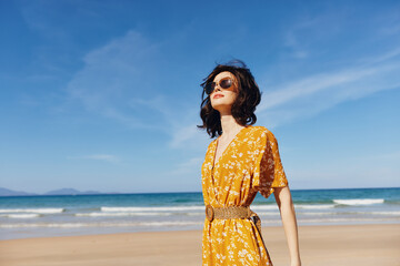 Woman in a vibrant yellow dress standing on sandy beach with scenic ocean view in background