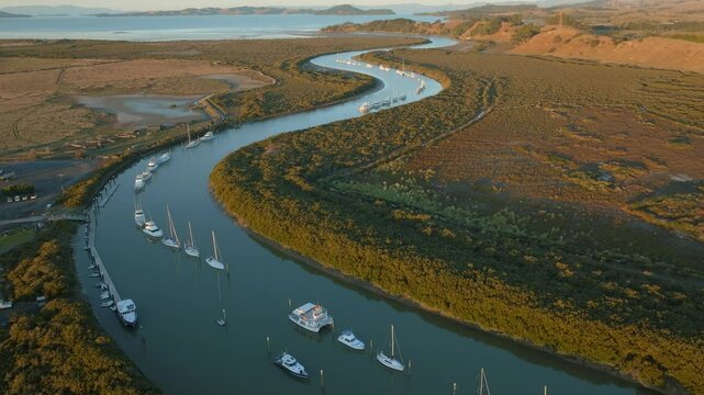 Aerial view of boats moored in a river, surrounded by lush greenery and mudflats, leading to the ocean in New Zealand. The scene captures the serene beauty of coastal life. CLEVEDON, NZ