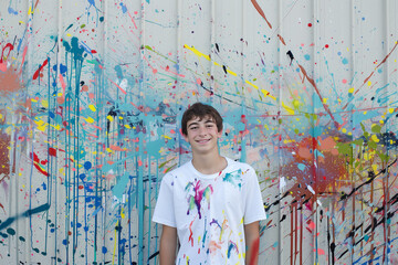Teenager standing in front of a mural they have painted, covered in paint splatters. Generative AI