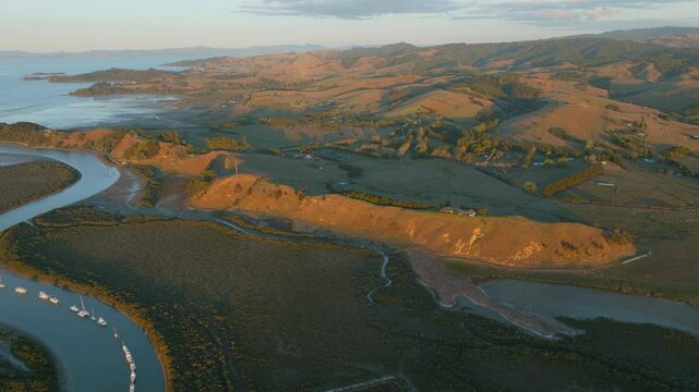 Aerial view of boats moored along the riverbank at sunrise in New Zealand. The boats are docked for recreational use and transport. The sun rises over the landscape. CLEVEDON, NZ