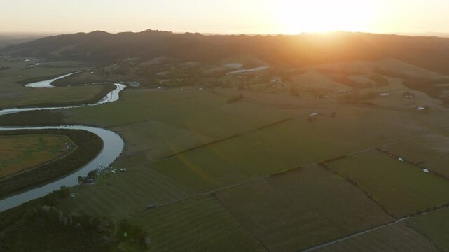 Aerial view of boats moored along the riverbank at sunrise in New Zealand. The boats are docked for recreational use and transport. The sun rises over the landscape. CLEVEDON, NZ