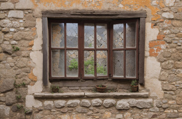 An old wooden window framed by a stone wall, with a small pot plants on the sill, creates a charming scene.