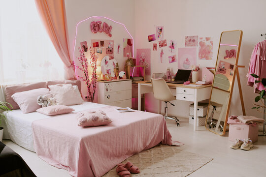 Wide shot of spacious bedroom of teen girl, room decorated with pink posters, neon led lights and wooden furniture