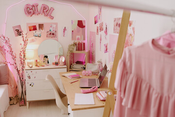 High angle shot of workplace in teen girl bedroom decorated with wooden furniture, pink posters and cherry blossom in crystal vase