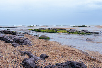 River mouth coming to the sea in a beach with people walking on a rainy day