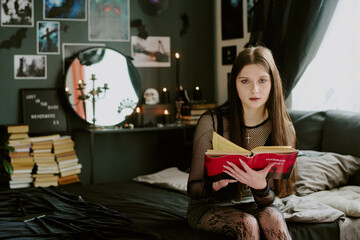 Medium shot of adorable goth teen girl with dramatic make-up dressed in total black holding red...