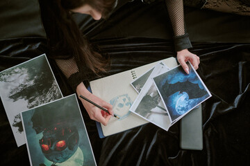 High angle shot of unrecognizable goth teenager lying on bed with black velvet linen drawing skull...