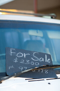 For Sale sign stuck under a windscreen wiper of a cheap car