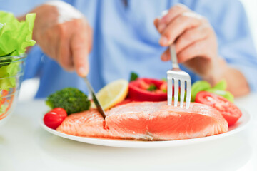 Asian elderly woman patient eating salmon stake and vegetable salad for healthy food in hospital.