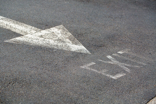 Faded white arrow painted on bitumen road