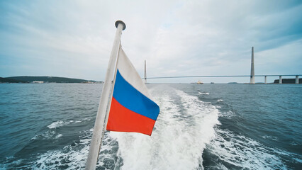 Russian flag waving proudly from a boat sailing near the iconic russky bridge in vladivostok,...