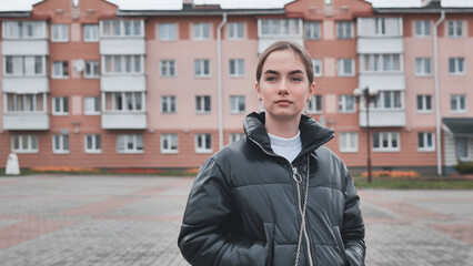 Trendy female standing in urban setting, black puffer jacket framing modern residential backdrop