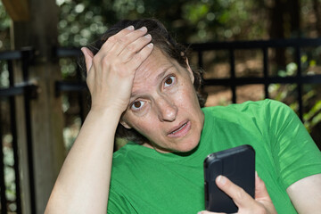 A scared pale woman looks at the camera after seeing bad news on her phone. Negative emotion concept.