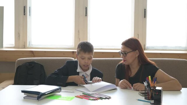 A homeschooled schoolboy does his homework with mom at desk. boy studies with a tutor at home