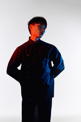 A handsome young man stands confidently, showcasing his stylish outfit with artistic lighting.