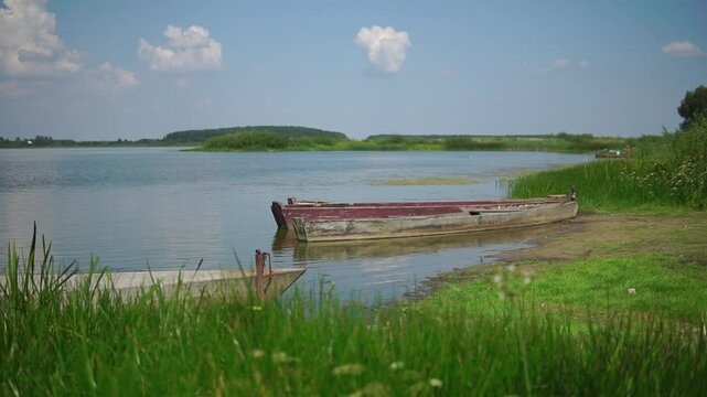 Old retro wooden boats docked at a river shore with green grass and a blue sky
