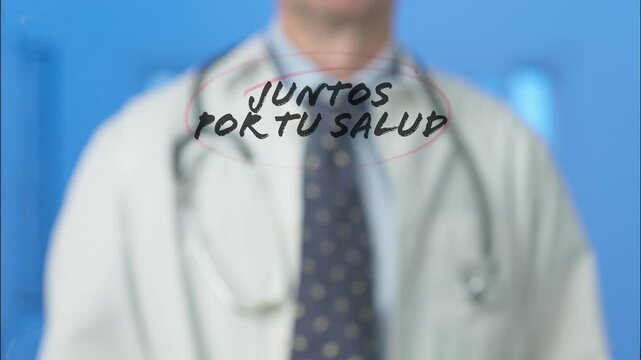 Doctor writing and circling in red the spanish words juntos por tu salud - together for your health - on a transparent board, isolated on a blue background
